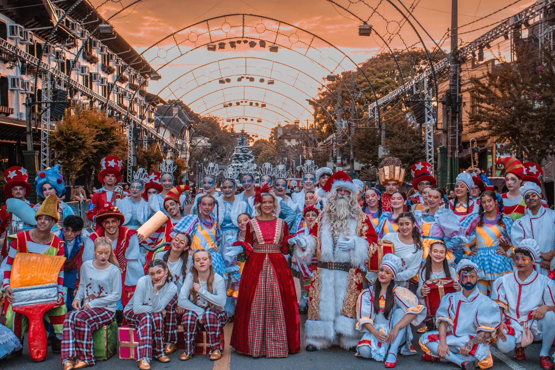 Elenco de Natal da FMN reunido com Papai Noel e Mamãe Noel sob os arcos de luz ao pôr do sol